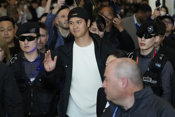 Los Angeles Dodgers' Shohei Ohtani waves as he walks with security guards during the baseball team's arrival at Incheon International Airport on Friday. [AP/YONHAP]