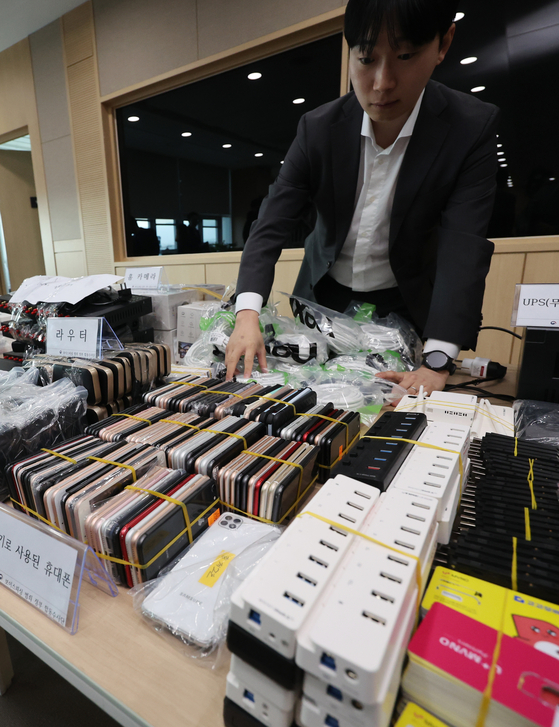 An official inspects phones used for voice phishing scams at the Seoul Eastern District Prosecutors' Office on Wednesday. The government arrested and charged 21 people for scamming. [YONHAP]