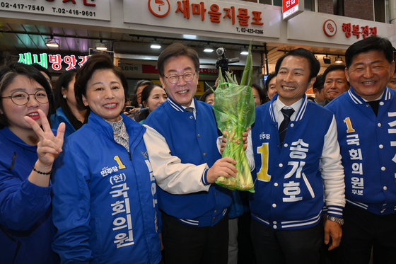 Democratic Party leader Lee Jae-myung poses with a green onion at a traditional market in Songpa District, southern Seoul, on Sunday. [NEWS1]