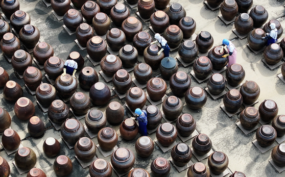Workers dust off the lids of large jangdok earthenware jars, which are used to ferment and store food, at a farm in Anseong, Gyeonggi, on Wednesday amid warm spring weather. [NEWS1]