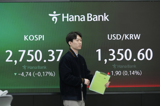 A currency trader moves by the screens showing the Kospi, left, and the foreign exchange rate between U.S. dollar and Korean won in the foreign exchange dealing room of the KEB Hana Bank headquarters in Seoul, Korea, Thursday. [AP/ YONHAP]