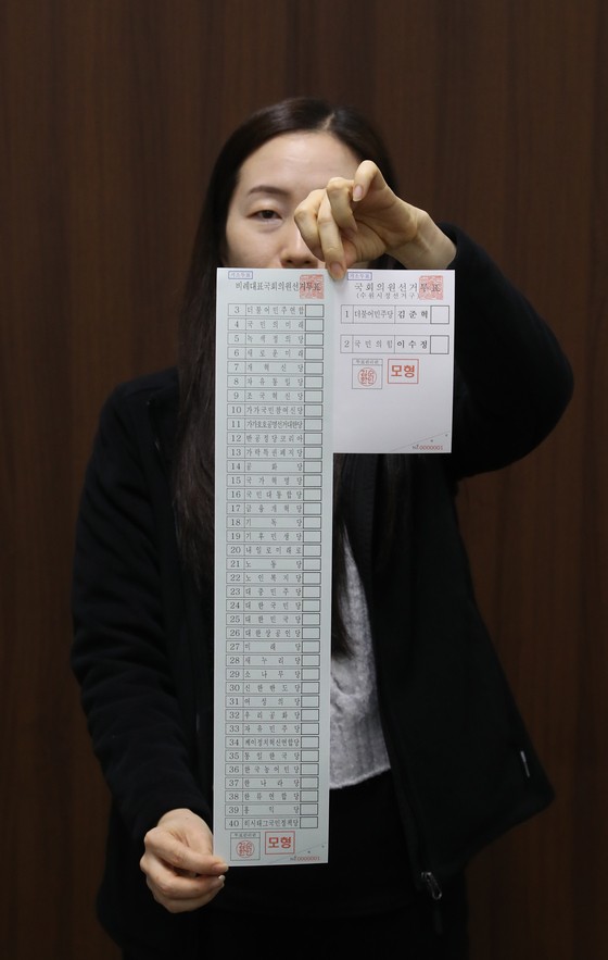 A National Election Commission official holds up a ballot paper for parties running for National Assembly seats filled by proportional representation next to a ballot paper for regional constituencies, where lawmakers are elected by first-past-the-post voting. In most regional constituencies, only candidates from the People Power Party and the Democratic Party are facing off. The competition is significantly stiffer for seats selected by proportional representation, for which the ballot paper this year measures 51.7 centimeters (20.3 inches), the longest in Korean history. [YONHAP]