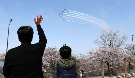 A family views the Korean Air Force’s Black Eagles aerobatic team soaring over Mapo Bridge in western Seoul during an air show celebrating the Yeongdeungpo Yeouido Spring Flower Festival on Sunday with cherry blossom season in bloom. The annual cherry blossom festival kicked off on Friday and runs through Tuesday. [NEWS1]
