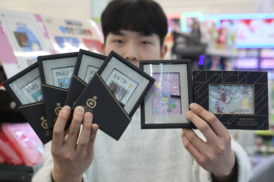 An employee at a branch of CU in Gangnam District, southern Seoul, holds the convenience store chain's new gold products on Sunday. Starting Monday, customers can purchase cards embedded with gold in-store. [YONHAP]