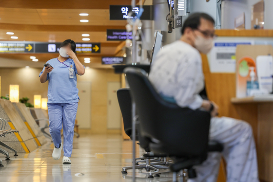A patient, right, sits on a chair in a general hospital in Seoul Sunday, as a medical professional walks by. [YONHAP]