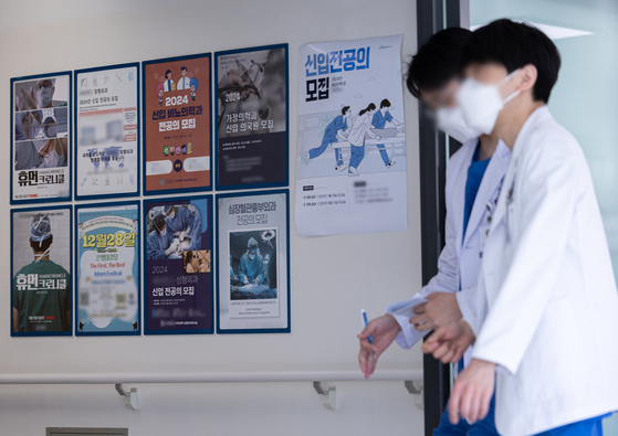 Medical professionals walk past a wall with recruitment posters for junior doctors at a general hospital in Seoul on Tuesday. [NEWS1]