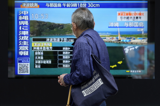 A passerby stands along a sidewalk to watch a television screen showing breaking news on tsunami warnings issued for the Okinawa region Wednesday. [AP/YONHAP]