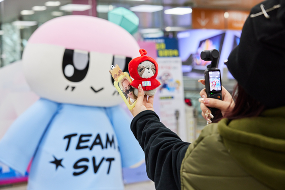 A fan of Seventeen, or Carat, takes photos in front of Seventeen's mascot, Bongbong, at the lounge prepared for guests taking Seventeen themed trains. [HYBE]