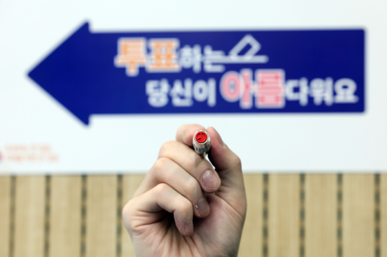 An election official holds up a voting stamp in front of a polling station in Yeongdeungpo District, western Seoul, on the eve of Korea's general election on Tuesday. [YONHAP]