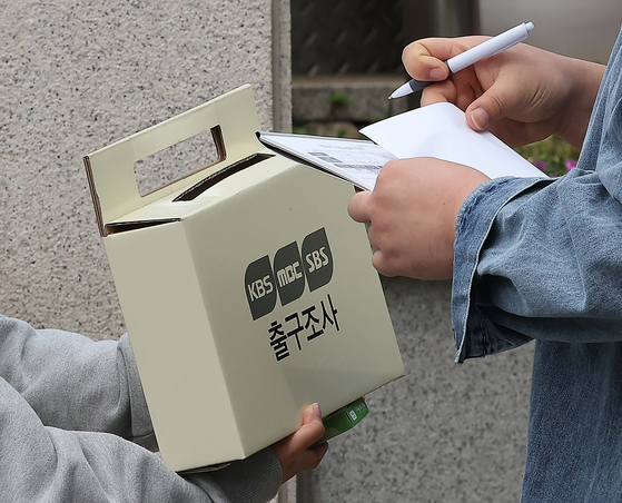 A pollster hands out gifts to voters who respond to an exit poll being conducted jointly by the three major broadcasters in front of a polling station at Yonsei University in Seodaemun District, central Seoul, Wednesday. [NEWS1]