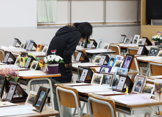 A person looks at photos of victims of the Sewol ferry tragedy at a classroom of Danwon High School in Ansan, Gyeonggi, on Monday. Tuesday marks the 10th anniversary of the tragedy, where 304 passengers and crew died after the Sewol ferry capsized off the coast of Jindo, South Jeolla, on April 16, 2014, while en route to Jeju Island. Of those who died on the ferry, 250 were juniors from Danwon High School. [YONHAP] 