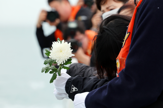 A family member of the Sewol ferry tragedy victim sobs while holding onto a white Chrysanthemum on a ship off the coast of Jindo County in South Jeolla on Tuesday. [YONHAP]