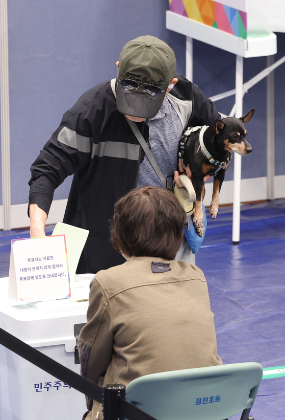 A voter juggles his dog and leash in one hand and casts his ballot with the other at a polling station installed at an elementary school in Songpa District, southeastern Seoul, on April 10. [YONHAP]