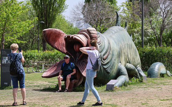 Foreign tourists take photos with the sculpture of the monster featured in the 2006 Korean film ″The Host″ at Hangang Park in Yeouido, western Seoul, on Thursday. The Seoul Metropolitan Government said the same day it will decide on the removal of the sculpture after holding a meeting with a public art review committee next month. [NEWS1] 
