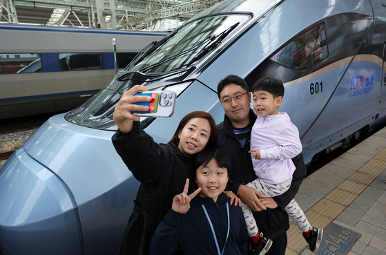 A family takes a photo in front of the KTX Cheong-ryong bullet train at Seoul Station in Jung District, central Seoul during a test run on Monday. [NEWS1]