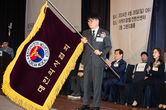 Lim Hyun-taek, president-elect of the Korean Medical Association, holds the group's flag at a general assembly meeting in Seocho District, southern Seoul, on Sunday. [NEWS1]
