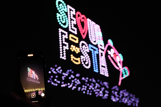 A visitor takes a photo of drones making the Seoul Festa logo at Jamsil Hangang Park in Songpa District, southern Seoul, on Saturday. [YONHAP] 