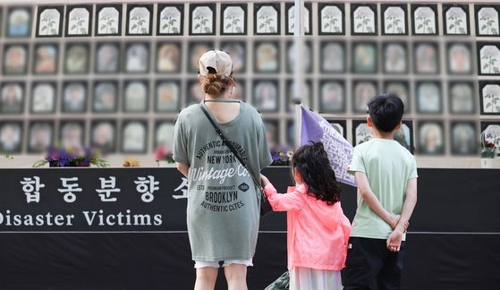  A mother and her two children pause in front of memorial altar to honor victims of the 2022 Itaewon crowd crush set up outside Seoul City Hall on Wednesday. [YONHAP]