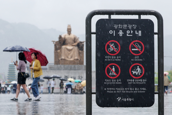 A no-smoking sign is seen as people walk in the rain in Gwanghwamun Square in Jongno District, central Seoul, on Sunday, during a three-day weekend to mark Children’s Day. The Constitutional Court recently ruled that the National Health Promotion Act, which requires all public facilities, including outdoor spaces, to be designated as non-smoking areas, does not violate the Constitution. The no-smoking icon was added to signposts this day. [YONHAP]