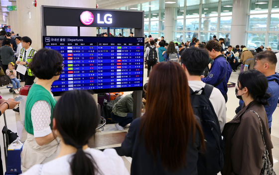 Travelers look at the departures board at Jeju International Airport on Sunday, as dozens of flights were canceled due to heavy rain and adverse weather conditions during the long weekend. [YONHAP]