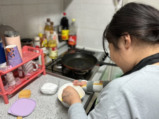 Koo Hye-bin, an 11-year-old family caregiver, prepares to cook eggs with her left hand as her right hand was injured to a recent fall last Thursday. [LEE BO-RAM]