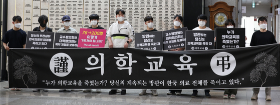 Students and junior doctors at Gyeongsang National University’s medical school and affiliated hospital hold a black funerary banner intended to symbolize the “death of medical education” as they stage a protest against the government’s plan to increase the annual medical school admissions quota on Wednesday in Jinju, South Gyeongsang. [YONHAP]