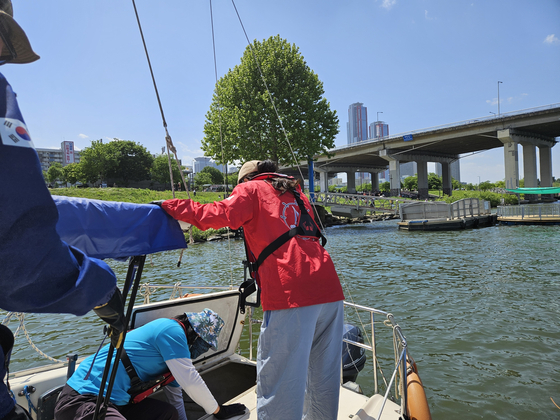 Mary grips onto the boom as Hyun checks the fuel tank. [SAILING PARADISE]