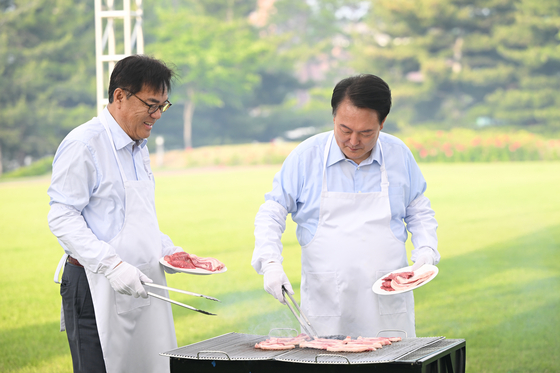Presiden Yoon Suk Yeol, kanan, memanggang daging babi bersama kepala stafnya Chung Jin-suk saat makan malam dengan korps pers di halaman kompleks kantor kepresidenan Yongsan di pusat kota Seoul pada hari Jumat. [PRESIDENTIAL OFFICE]