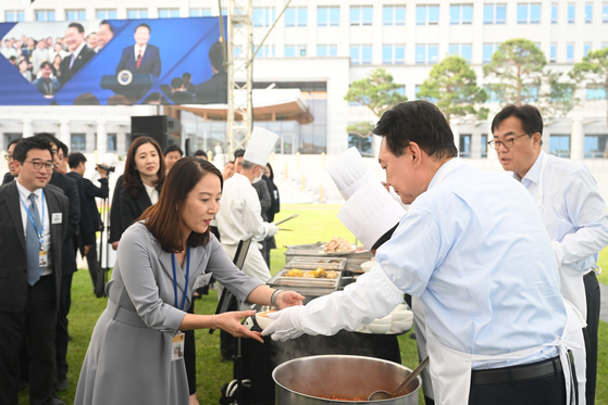 President Yoon Suk Yeol, right, ladles kimchi stew for reporters during a rare dinner with the presidential press corps at a lawn at the Yongsan presidential office compound in central Seoul Friday. [PRESIDENTIAL OFFICE]