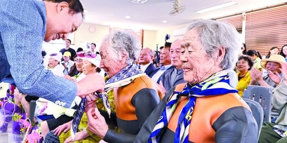 Yang Young-cheol, the chief director of Jeju Free International City Development Center, presents scarfs to nine retiring haenyeo, including the 92-year-old Kim Yoo-sang, at the first retirement ceremony honoring haenyeo at a community center of Gwideok 2-ri fishing village. [YONHAP]