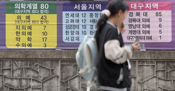  Students stroll past a banner in Suseong District, Daegu, displaying the number of students admitted to various medical schools and prestigious institutions. [YONHAP]