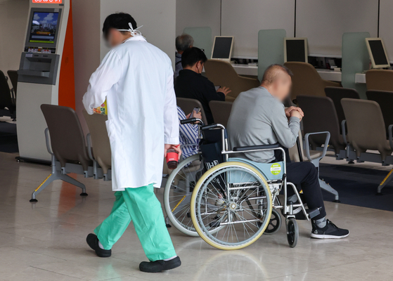 A doctor walks past a patient on a wheelchair in a general hospital in Seoul on Thursday. [YONHAP] 