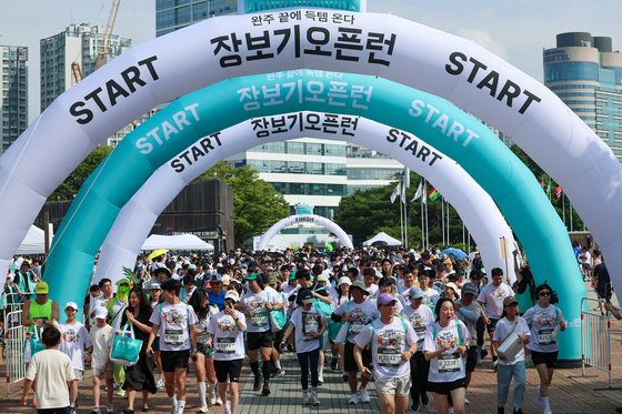 Participants of a grocery shopping marathon event hosted by Baedal Minjok, Korea's largest food delivery app, run while holding a grocery bag on Sunday at Olympic Park in eastern Seoul. The event allows participants to grab whatever item is on display at pop-up zones throughout the five-kilometer (three-mile) marathon route. Those who finish the course can keep what they have grabbed. Some 60,000 items ranging from food and beverages to daily necessities were up for grabs. [YONHAP]
