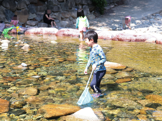  Children play in the water on Monday at Jangyu Daecheong Valley in Gimhae, South Gyeongsang, where a heat wave advisory was issued for the first time this summer. A heat wave advisory is issued when the apparent temperature is expected to be 33 Celsius (91.4 Fahrenheit) or higher for two consecutive days. [YONHAP]