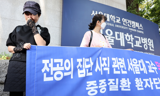 A cancer patient, left, sheds tears in a press conference requesting Seoul National University Hospital (SNUH) professors withdraw their plan to stage an indefinite walkout in front of SNUH in downtown Seoul on Wednesday. [NEWS1] 