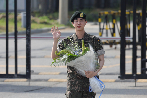 BTS's Jin, with a bouquet in his hand, waves at dozens of cameras on Wednesday as he gets discharged from the ROK Army 5th Infantry Division Recruit Training Center in Yeoncheon County, Gyeonggi, on Wednesday, after completing 18 months of his mandatory military service. [YONHAP] 