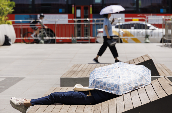A person covers their face and upper torso with a sun shade while lying on a bench in central Seoul on Wednesday. [YONHAP] 