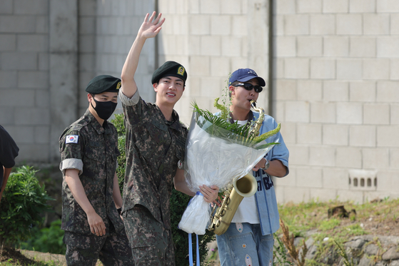 Jin waves to reporters on June 12 as he leaves the ROK Army 5th Infantry Division Recruit Training Center in Yeoncheon County, Gyeonggi, with bandmate RM playing the saxophone at his right. [YONHAP]