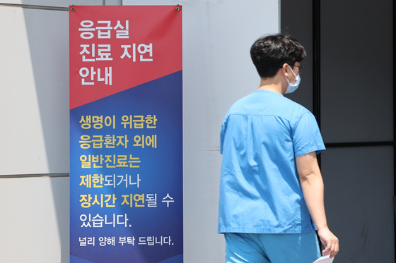 A medical worker enters the emergency center at Seoul National University Hospital in Jongno District, central Seoul, on Friday, passing a banner that notifies the postponement of treatment at the emergency room. [YONHAP]