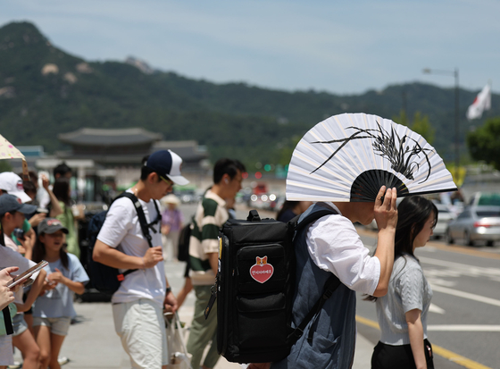 A passerby covers his face with a large fan in downtown Seoul as the capital experiences hot summer weather on Monday. Seoul's daily temperature peaked at 30.2 degrees Celsius (86.4 degrees Fahrenheit) the same day, according to the Korea Meteorological Administration. [YONHAP] 