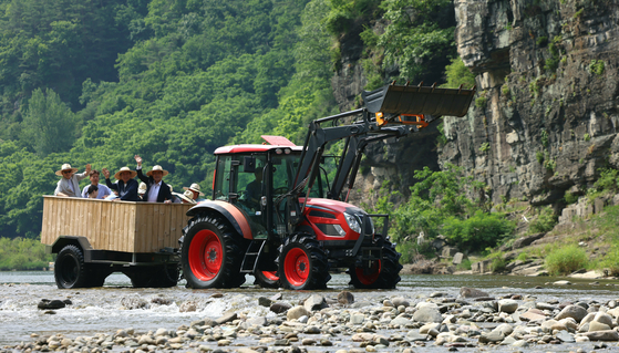 Culture Minister Yu In-chon and press ride a tractor through the Nakdong River on the way to Menge Village in Andong, North Geyongsang, on Thursday [MINISTRY OF CULTURE, SPORTS AND TOURISM]
