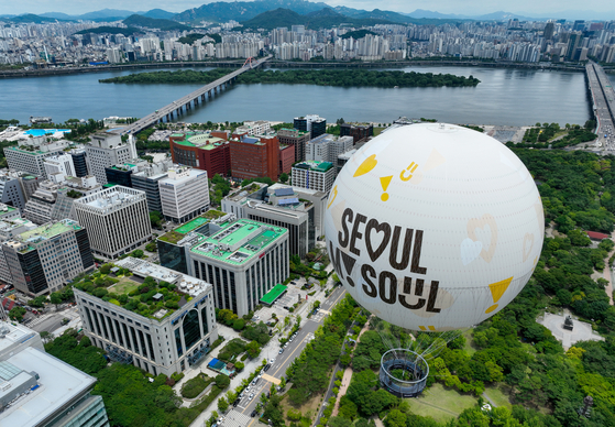  The “Moon of Seoul,” a moon-shaped tethered balloon, makes a test flight over Yeouido, western Seoul, on Sunday. Filled with helium gas, the balloon will undergo pilot runs through July and is scheduled to begin official operations for the general public in August. The balloon is seen with the city’s slogan,″”Seoul, My Soul.” It can float up to 150 meters (492 feet) and accommodate up to 30 passengers, allowing them to enjoy the city’s scenery. [YONHAP]