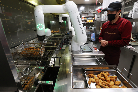 A worker supervises a chicken-frying robotic arm installed in a Kyochon store in Namyangju, Gyeonggi, in January 2023. [YONHAP]