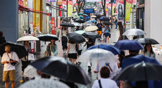 People holding umbrellas pass through a street in Myeong-dong, central Seoul, on Saturday. [YONHAP] 