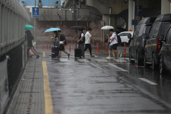 People with umbrellas cross the street as monsoon rain pours at Jeju International Airport on Jeju Island on Sunday. [YONHAP] 