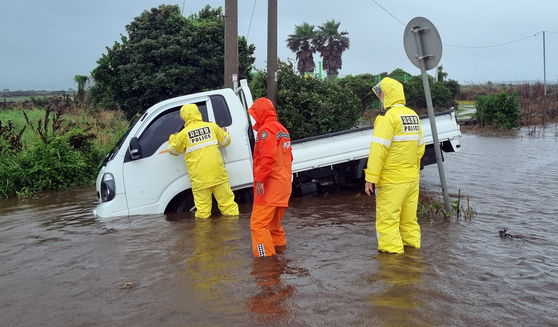 First responders conduct safety measures as a truck gets stuck on the road amid a flooding on Saturday on Jeju Island. [JEJU FIRE HEADQUARTERS]