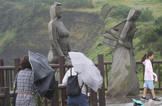 Visitors holding umbrellas walk on a mountain trail in Seogwipo, Jeju Island, on Sunday. A strong wind advisory was issued by weather authorities as heavy monsoon rain battered the island. [NEWS1]