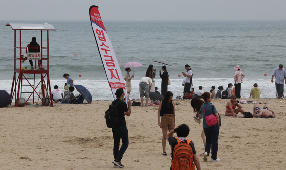 Beachgoers on Haeundae Beach in Busan sit and watch ocean waves as swimming is prohibited for safety purposes when a monsoon hit Jeju Island on June 23. [SONG BONG-GEUN]