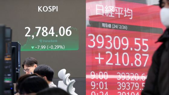 Left: An electronic board in central Seoul shows Korea's benchmark Kospi on June 27. Right: A person walks in front of an electronic screen showing Japan's Nikkei 225 index on February 26. [YONHAP/AP]