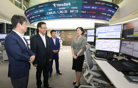 From left: Bank of Korea Senior Deputy Gov. Ryoo Sang-dai, Finance Minister Choi Sang-mok and Hana Financial Group Chairman Ham Young-joo speak with a trader at Hana Bank's trading room in central Seoul on Monday, the first official day of the extension of won-dollar trading hours. [HANA FINANCIAL GROUP] 
